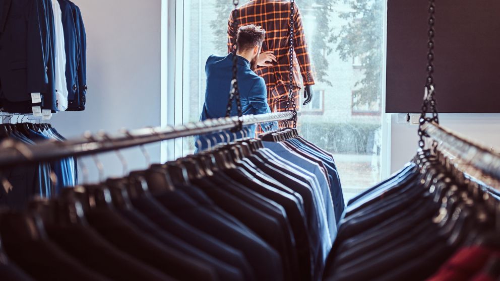 Stylish bearded seller care about suit on a mannequin in menswear store.