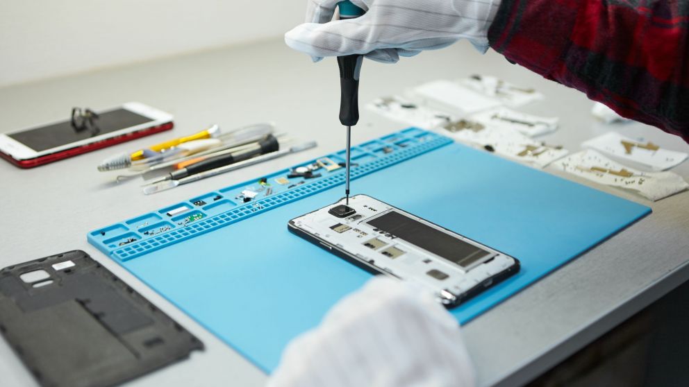 Repara celularCropped shot of male technician in antistatic gloves using screwdriver to disassemble borken mobile phone, going to repair motherboard, sitting at his workplace in laboratory with needed equipmentes (