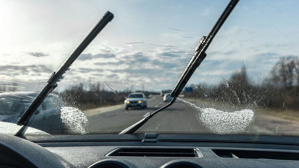 Car wipers clean windshields when driving in sunny weather, inside view.