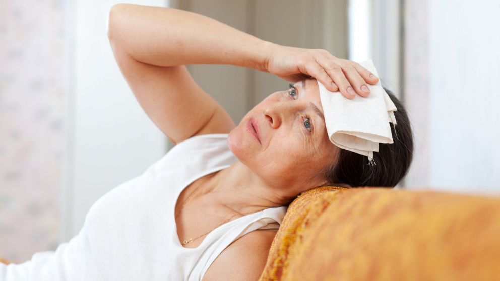sick mature woman having headache holding towel on her head
