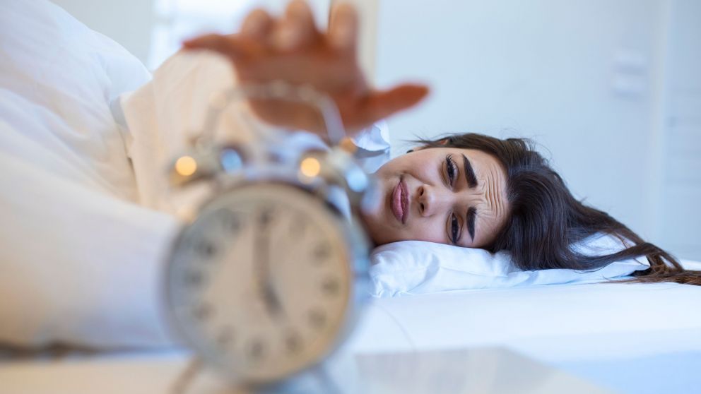 Woman lying in bed turning off an alarm clock in the morning at 5am. Hand turns off the alarm clock waking up at morning, girl turns off the alarm clock waking up in the morning from a call.