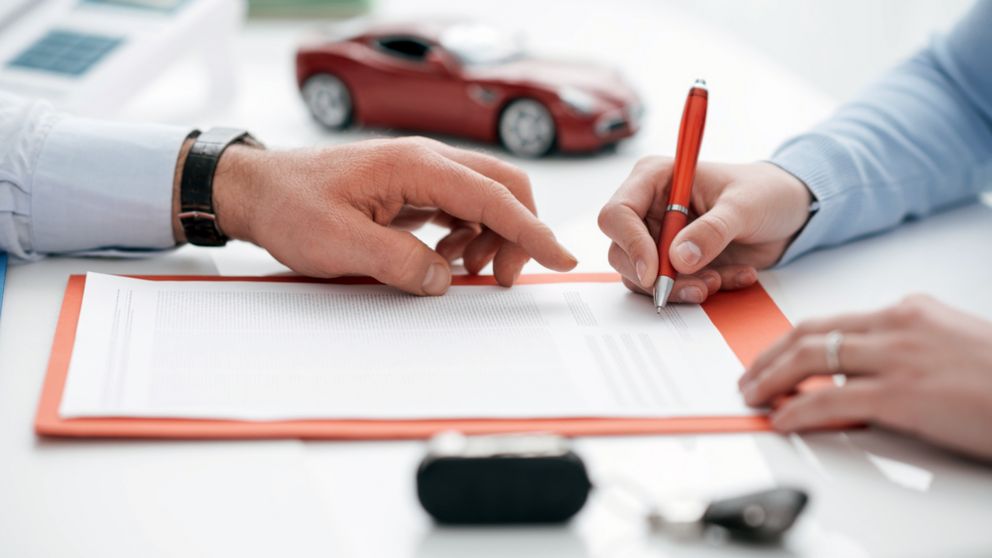 Woman signing a car insurance policy, the agent is pointing at the document